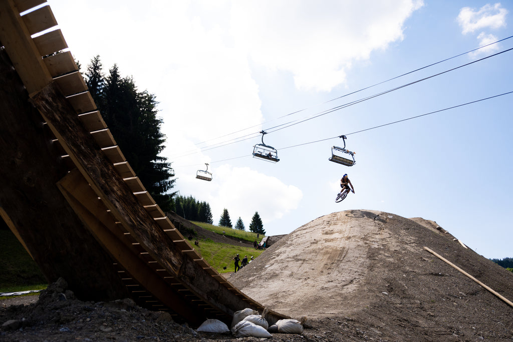 guy riding a mountian bike over dirt bike tracks and jumps with chair lifts in the background